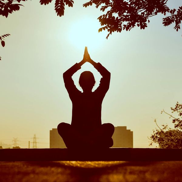 Person meditating peacefully outdoors at sunrise.